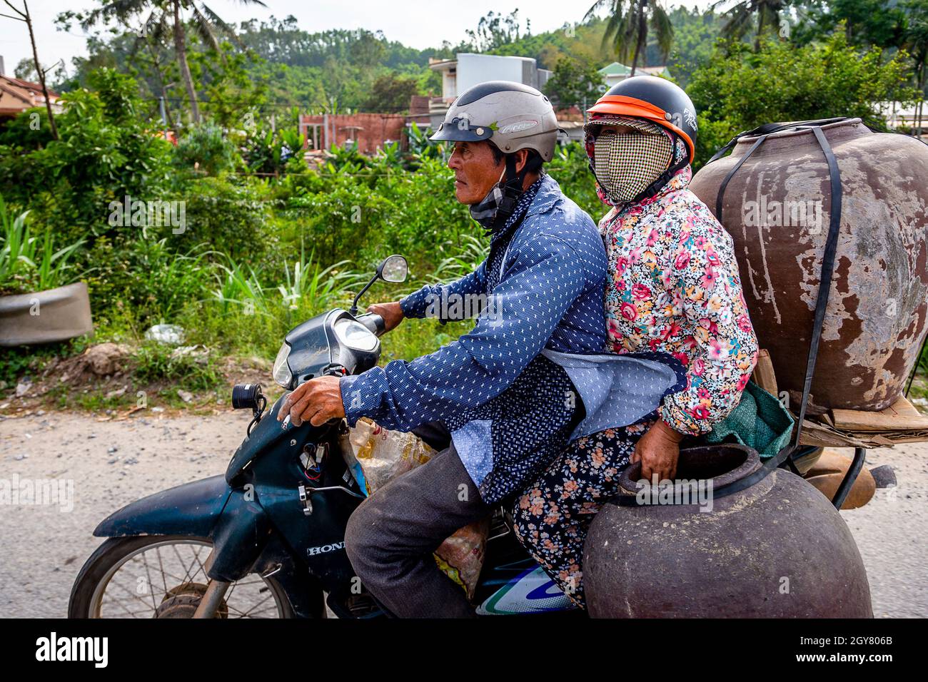 Due persone su una moto che trasportano grandi vasi per la consegna in autostrada in Vietnam. Vista laterale. Foto Stock