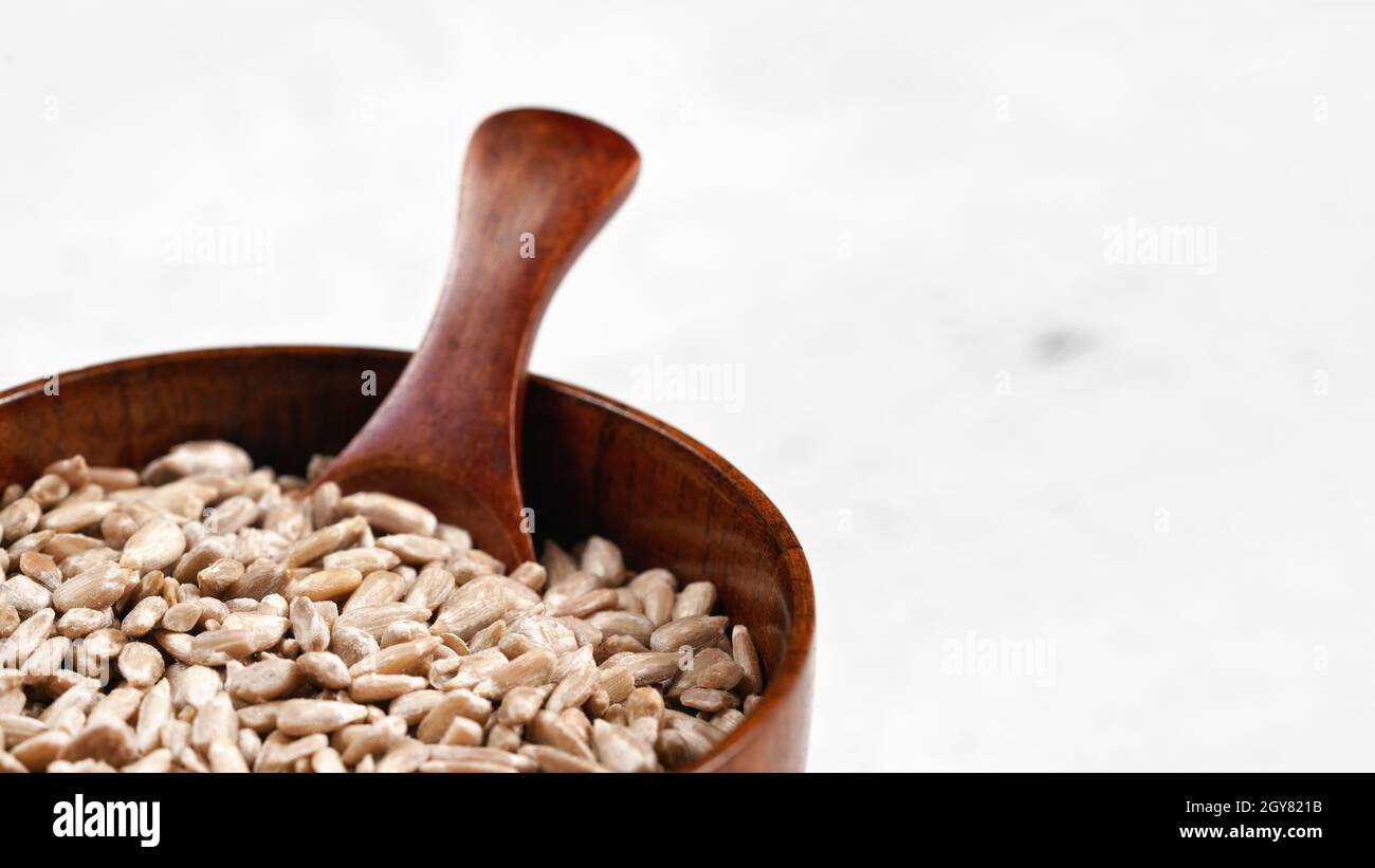 Semi di girasole sbucciati in una piccola ciotola di legno o in una tazza con cucchiaio sulla tavola bianca, spazio per il testo sul lato destro. Foto Stock