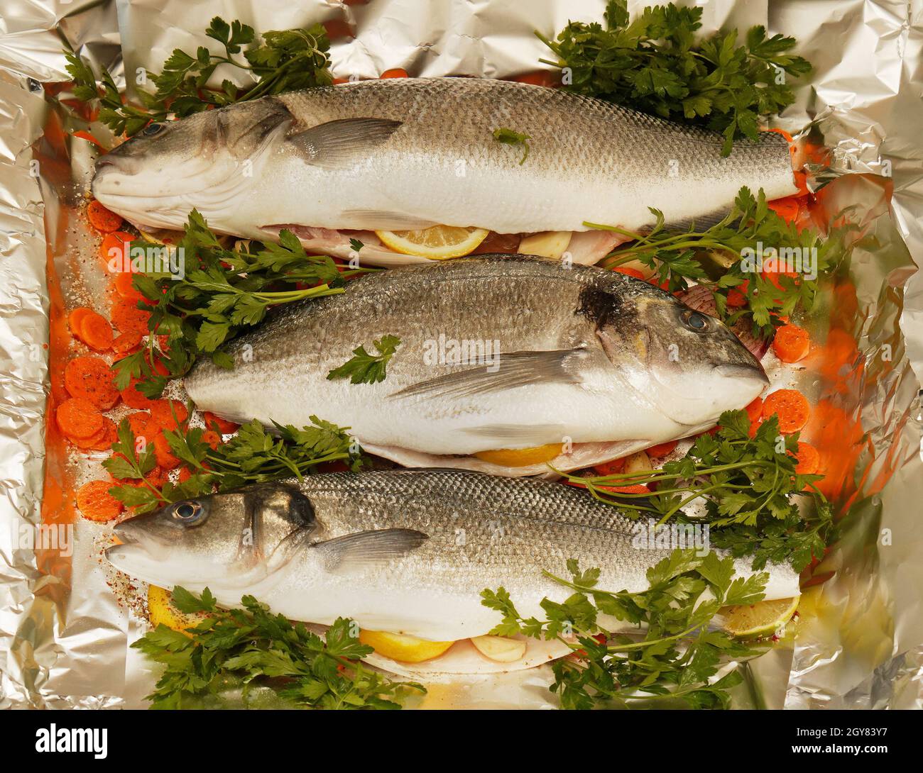 Spigola fresca e orata pronta per la cottura, lamina di alluminio con verdure Foto Stock