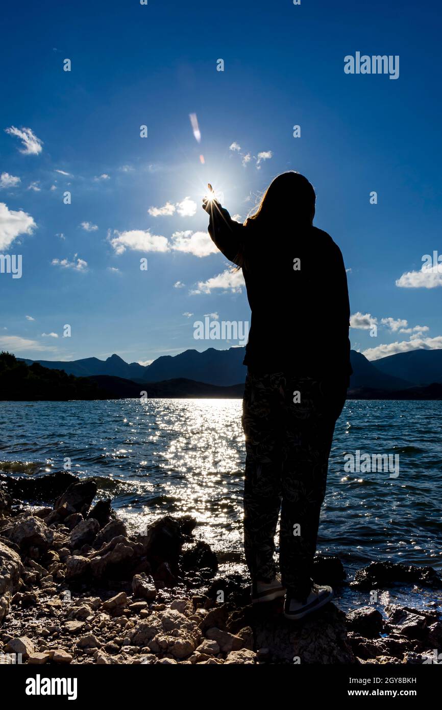 Silhouette di una donna matura spagnola che finge di toccare il sole sulla riva del bacino idrico di Porma a Castilla y Leon Spain.The foto mostra una f Foto Stock