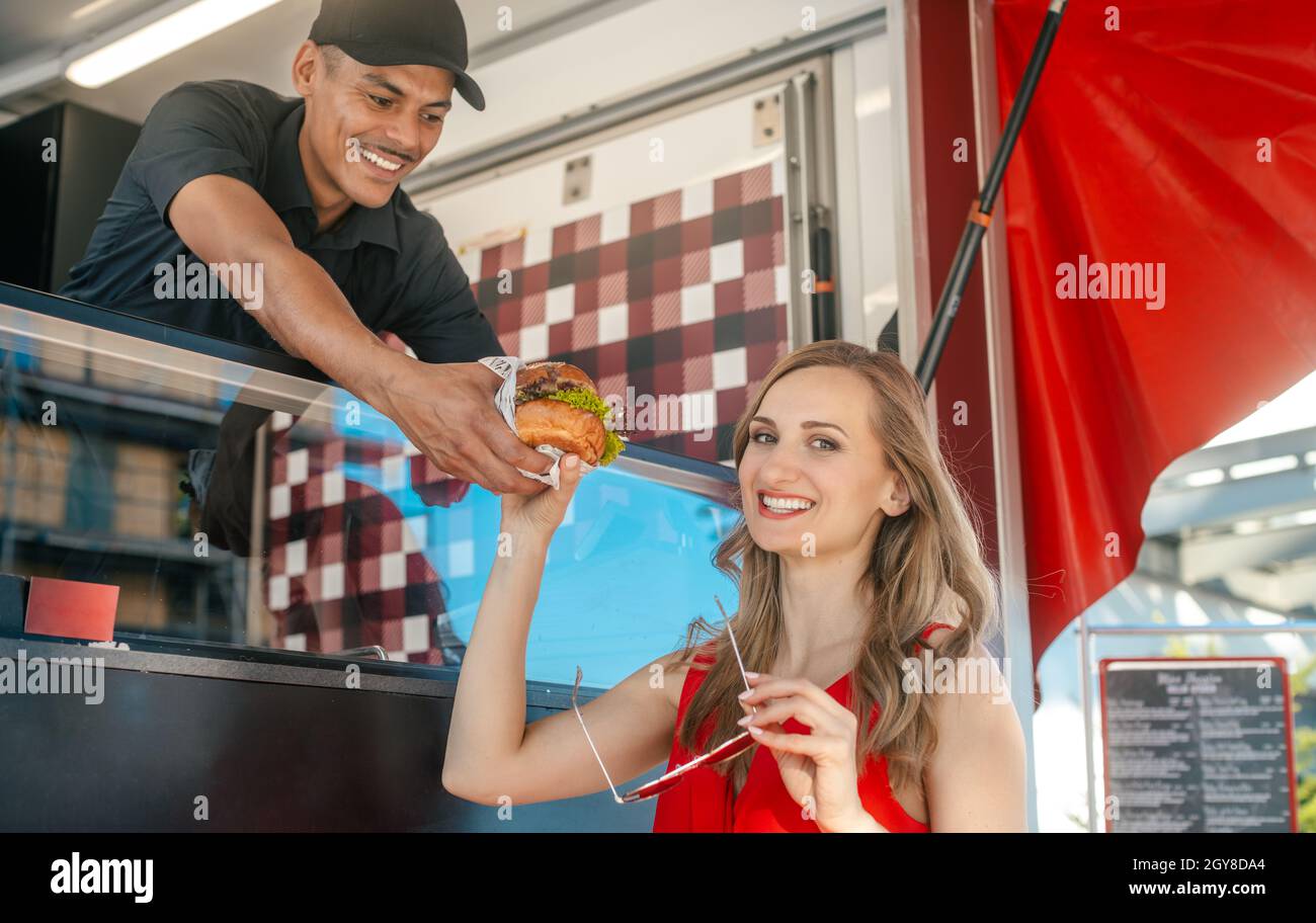 Bella donna che ottiene un hamburger come cibo da asporto dal cuoco in camion di cibo che la rende visibilmente felice Foto Stock