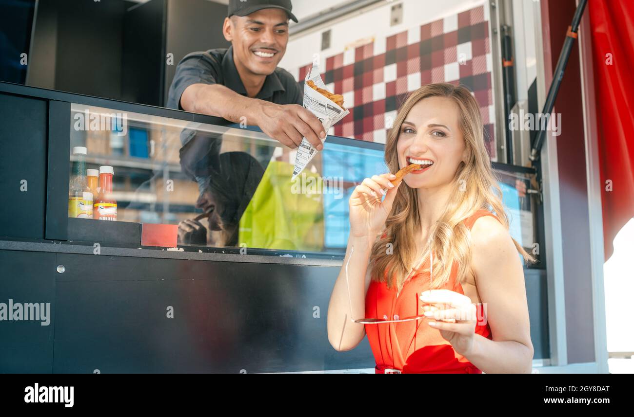 Bella donna che ordina patatine fritte a un camion di cibo prendendo un primo boccone Foto Stock
