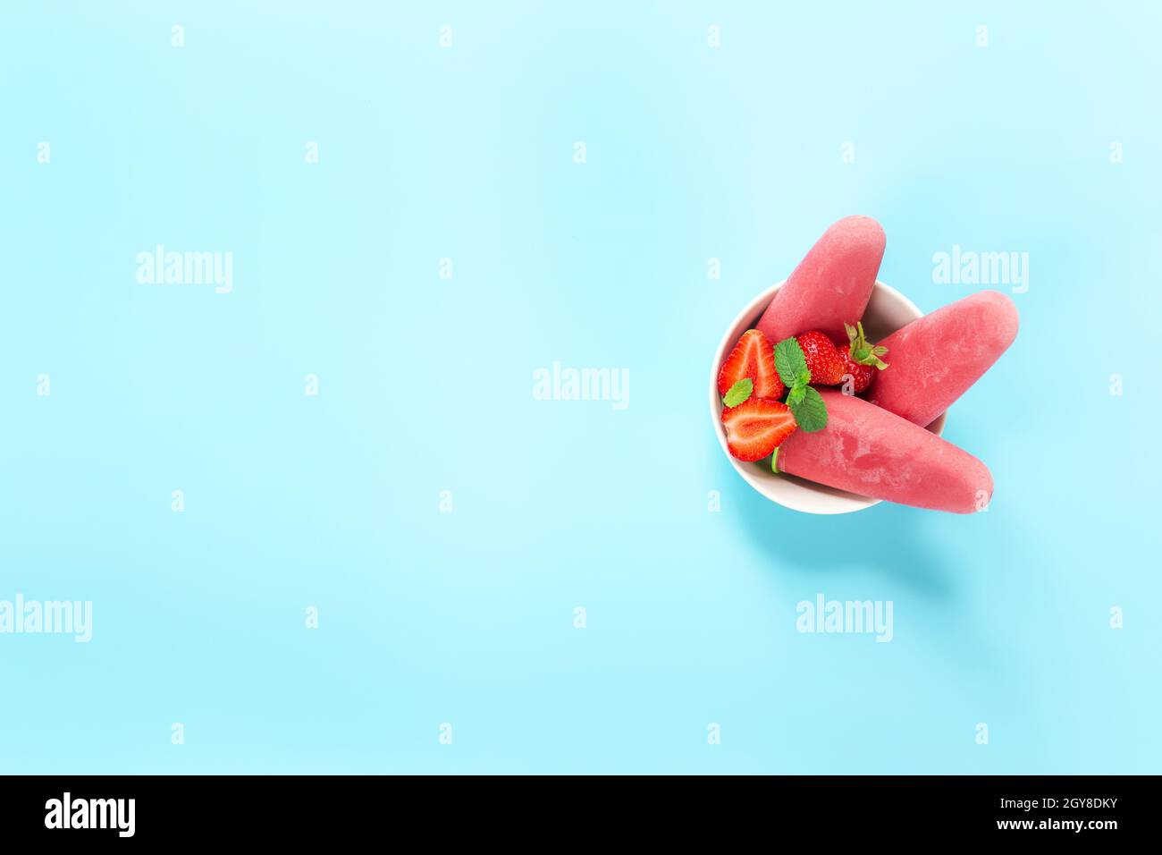 Vista dall'alto sulla ciotola con gelato al sorbetto congelato rosa fruttato su bastone di plastica con fragola, menta su sfondo blu. Frutta mista surgelata con yogurt i. Foto Stock