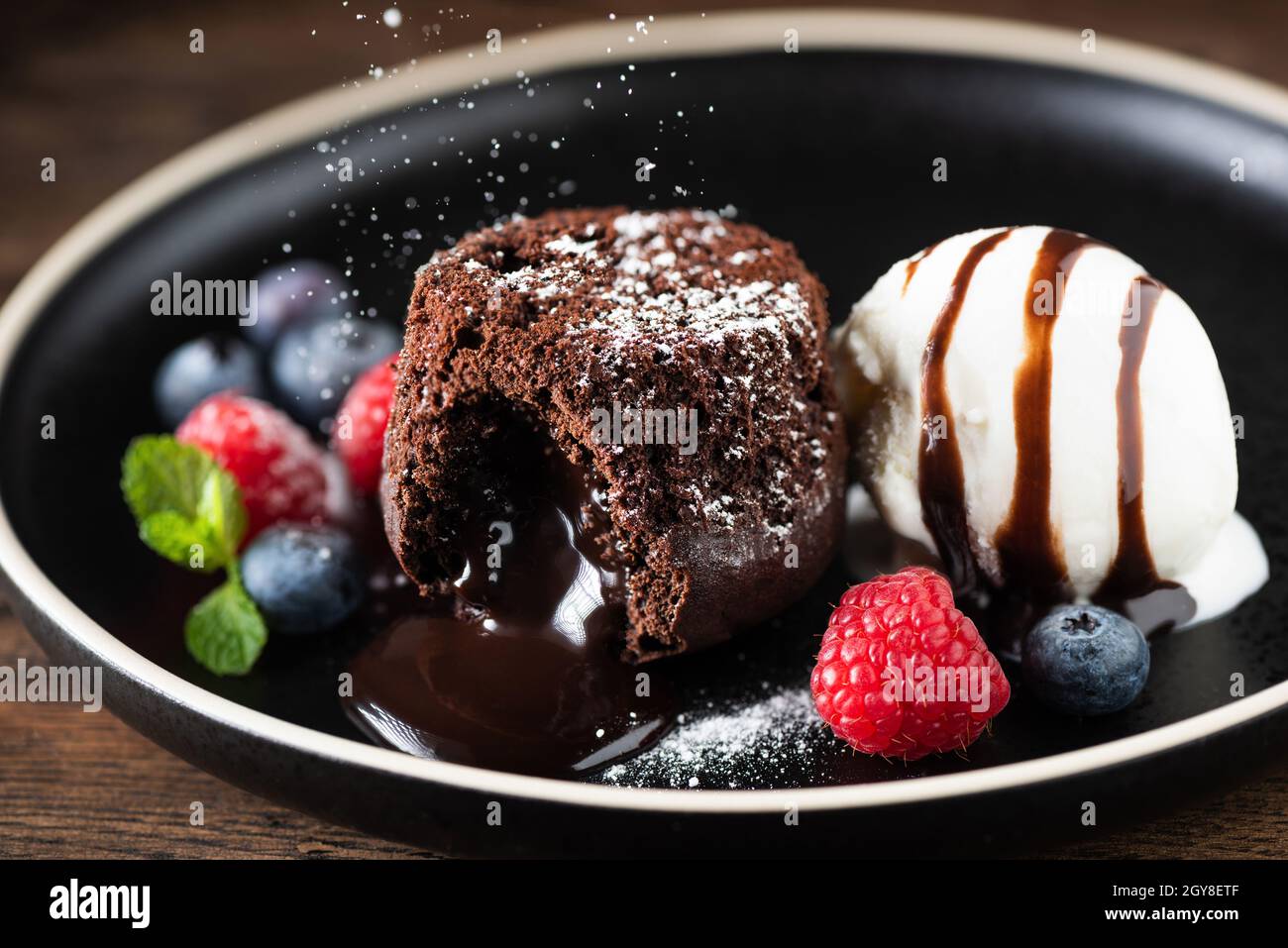 Torta al cioccolato fondente, torta di lava fusa con cucchiaio per gelato e bacche fresche sul piatto Foto Stock