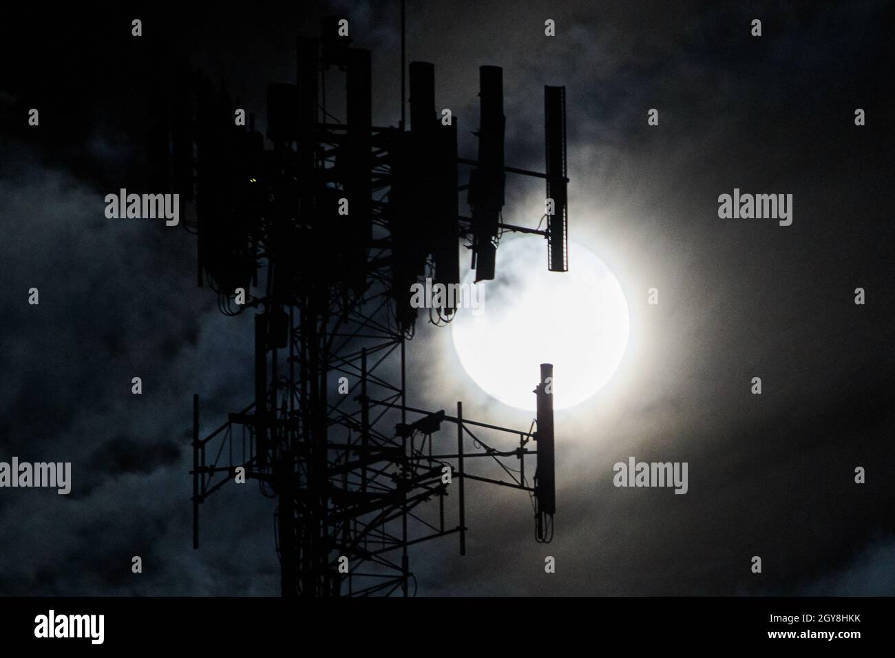 Mietete la luna piena bianca con una silhouette a torre davanti a essa e le nuvole spionde Foto Stock