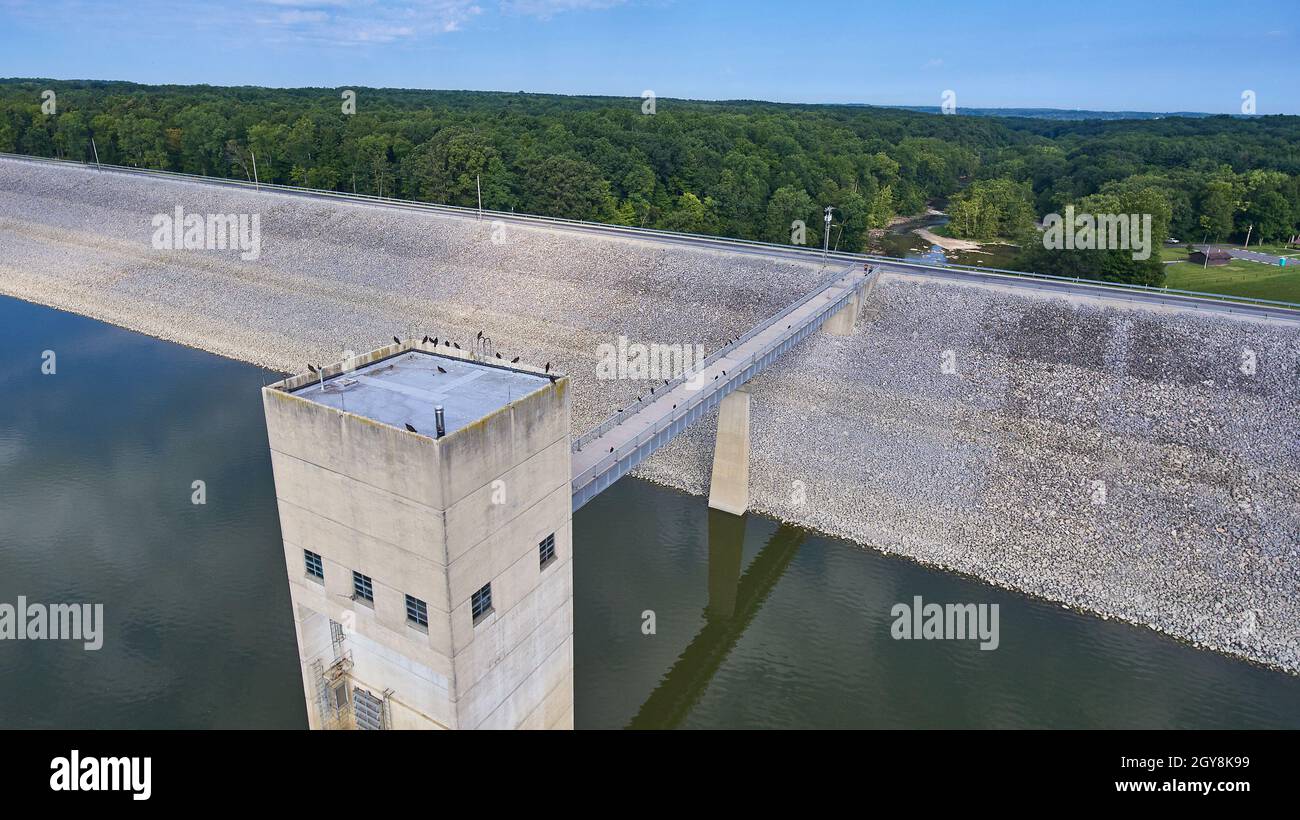 Antenna di una diga di cemento con pendii di ghiaia e corvi sulla zolla e sulla sposa e una foresta sullo sfondo Foto Stock