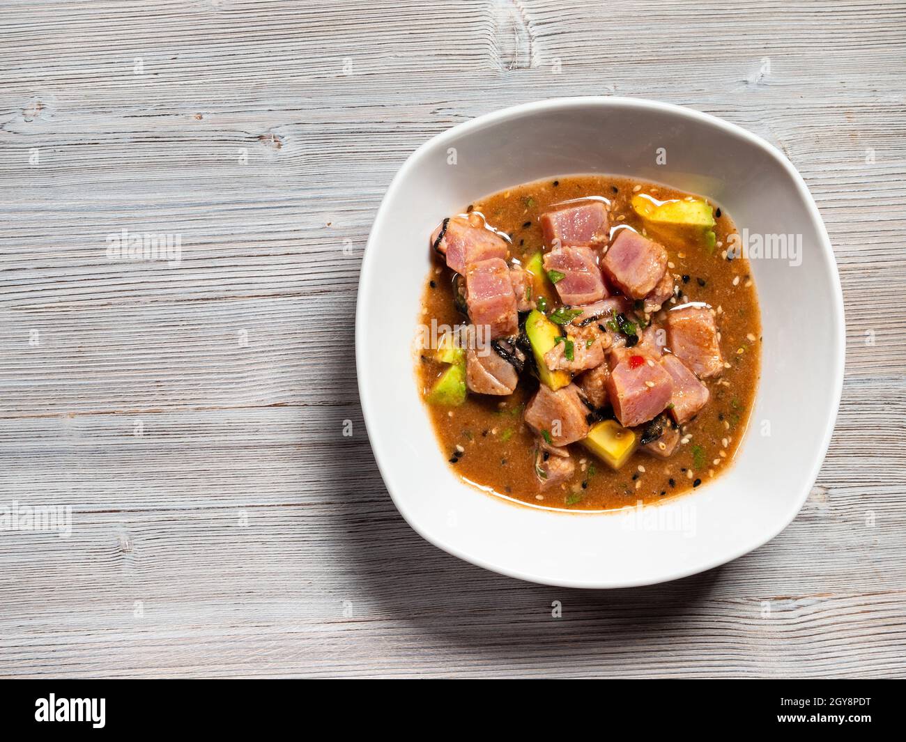 Vista dall'alto del tonno peruviano ceviche in salsa Tamarind con pezzi di avocado e alghe in ciotola su tavola grigia in legno con copyspace Foto Stock