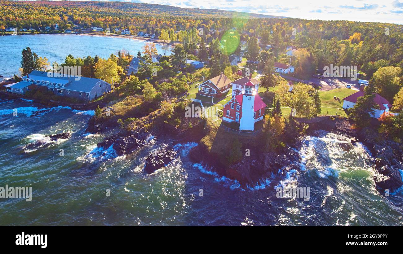 Faro con onde bianche un sole che fioca e uno scatto aereo del lago con alberi di caduta e la foresta sullo sfondo Foto Stock