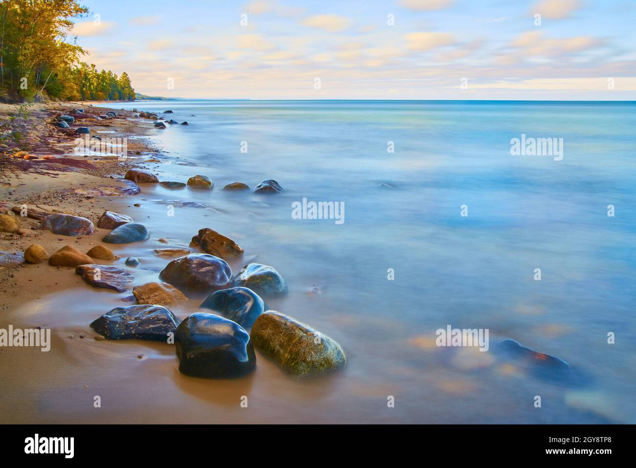 Misty lago superficie con rocce bagnate e lisce contro una spiaggia sabbiosa con una foresta Foto Stock