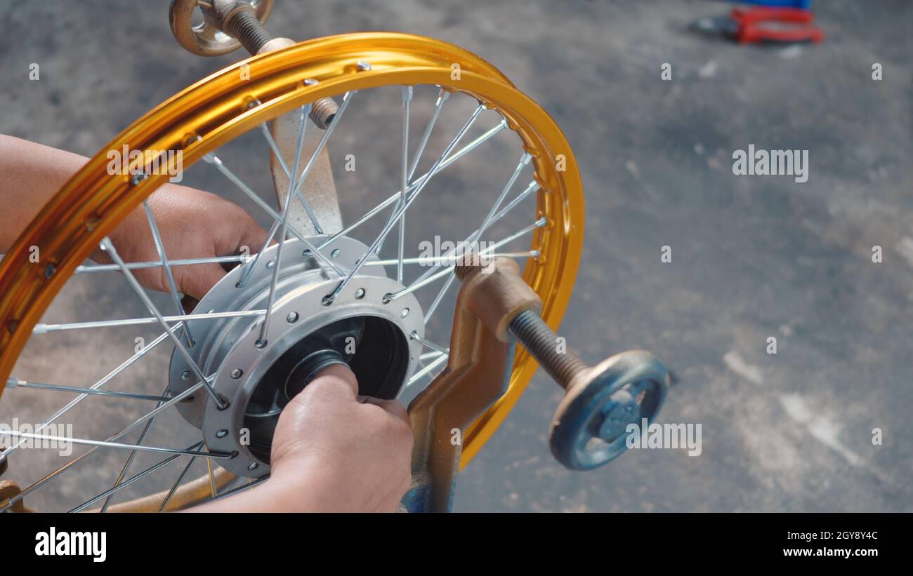 Il tecnico uomo che lavora la ruota del motociclo ha raggi che si intrecciano su nuova ruota in acciaio meccanica, motorcycle raggi ruota allineamento macchina utensile Foto Stock