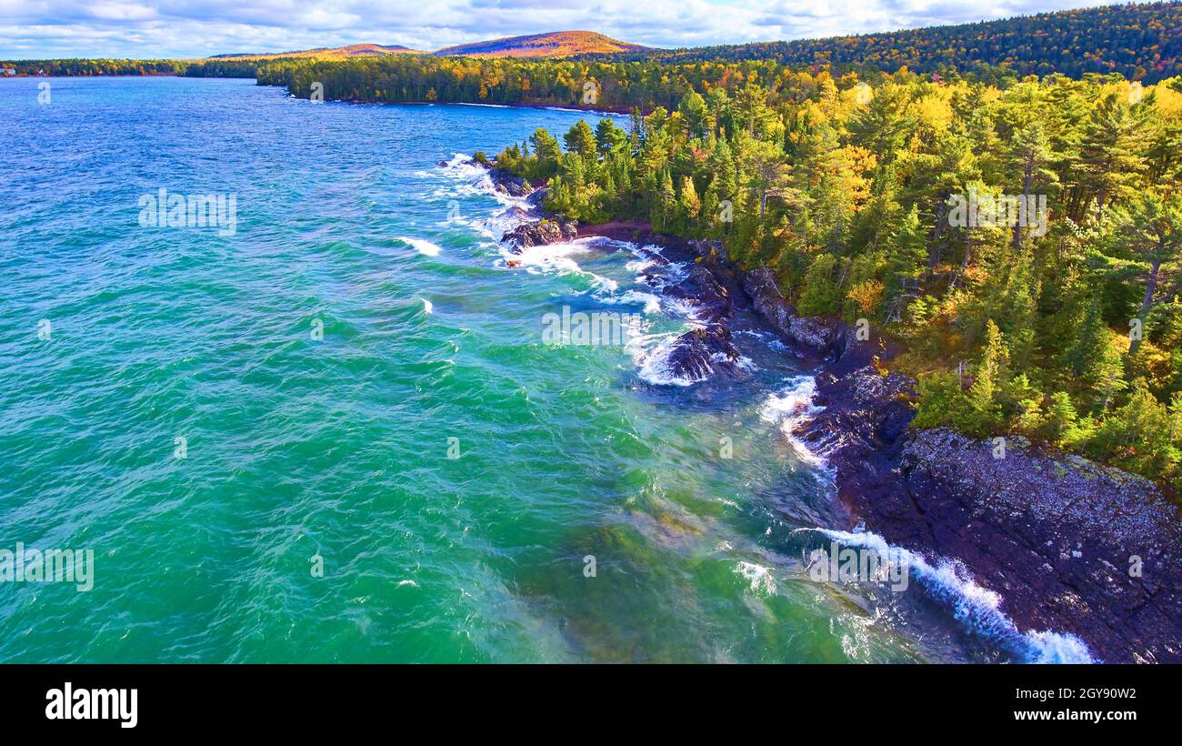 Acqua blu e teale di un lago o di un mare con una foresta di caduta e scogliere Foto Stock