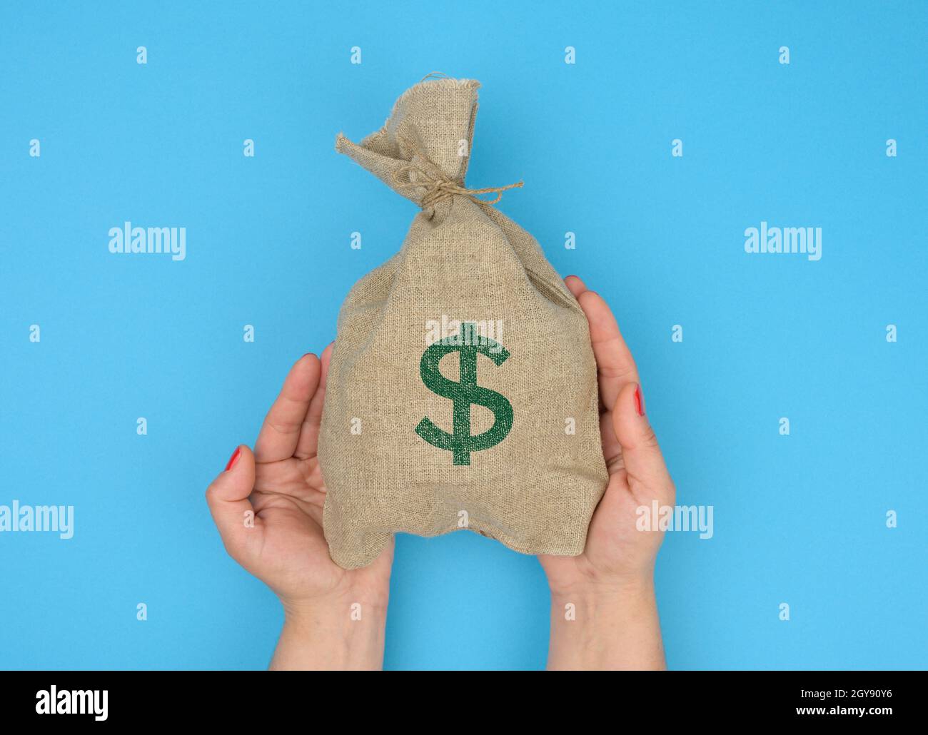 La mano tiene una borsa di tela piena di soldi con un'icona del dollaro degli Stati Uniti su uno sfondo blu. Concetto di pianificazione del bilancio, profitto e risparmio, risultato finanziario finale Foto Stock