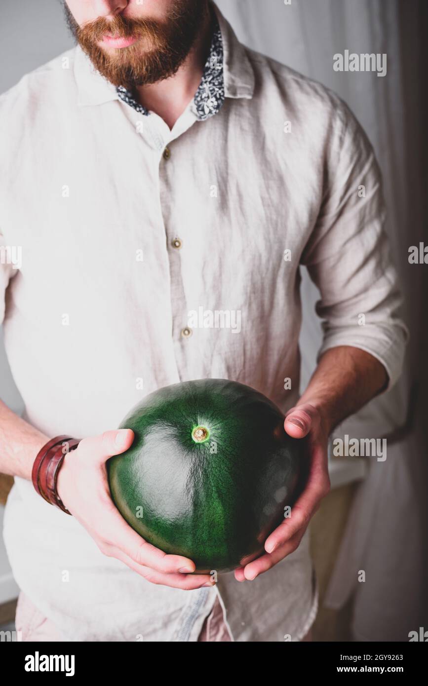 L'uomo portato in camicia di lino tiene nelle sue mani l'intero anguria verde Foto Stock