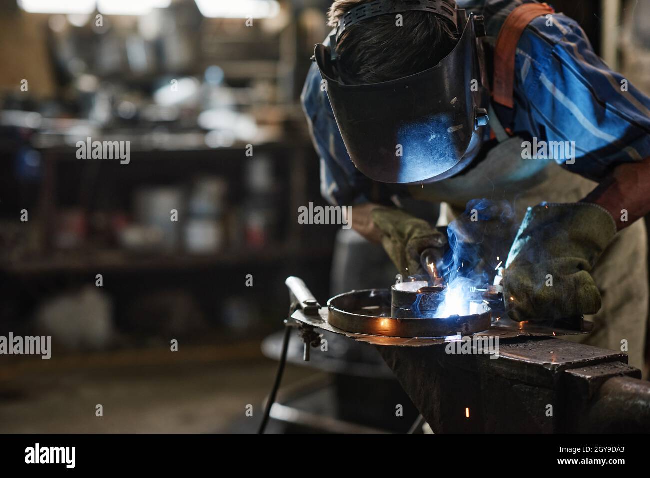 Operatore in maschera di protezione per la saldatura del metallo con attrezzatura speciale in officina Foto Stock