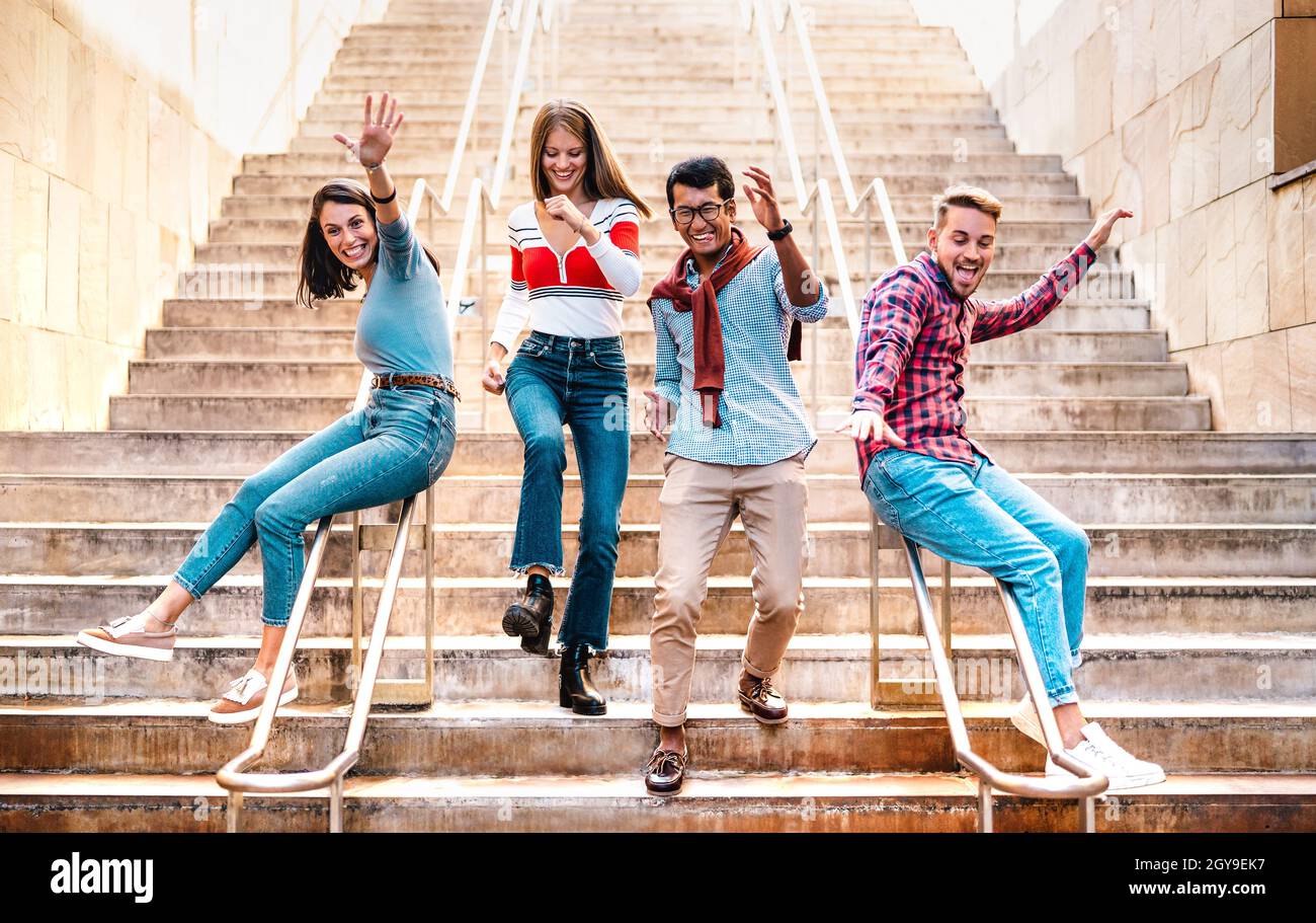 Amici multietnici che camminano giù le scale con stupidi mosse divertenti - ragazzi e ragazze felici che si divertono nel centro città urbano con l'umore del partito Foto Stock