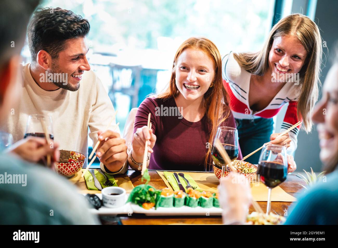 Amici felici che mangiano con i bastoni di pollo al ristorante sushi - cibo e bevande concetto di stile di vita con i giovani che si divertono insieme al bar Fusion Foto Stock