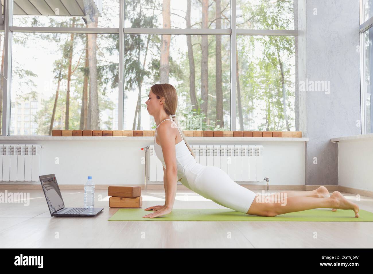 Giovane donna in forma sportiva che fa sport o yoga online con il laptop. Allenamenti a distanza, formatore online. Foto Stock