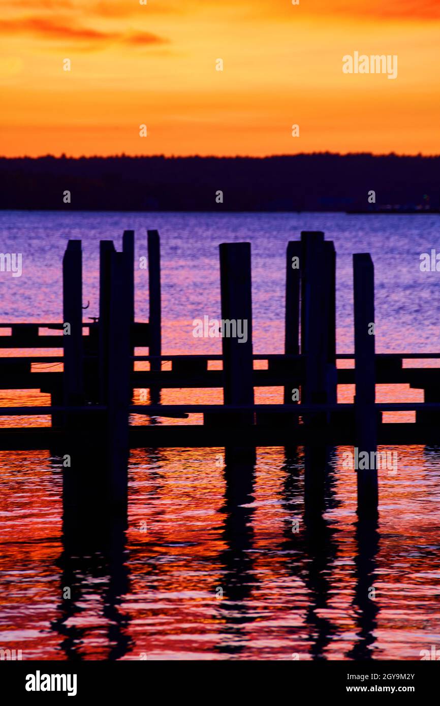 Ormeggia le sagome in un fiume di rosso e arancione viola con un cielo giallo e arancione e una linea di alberi contro il cielo Foto Stock