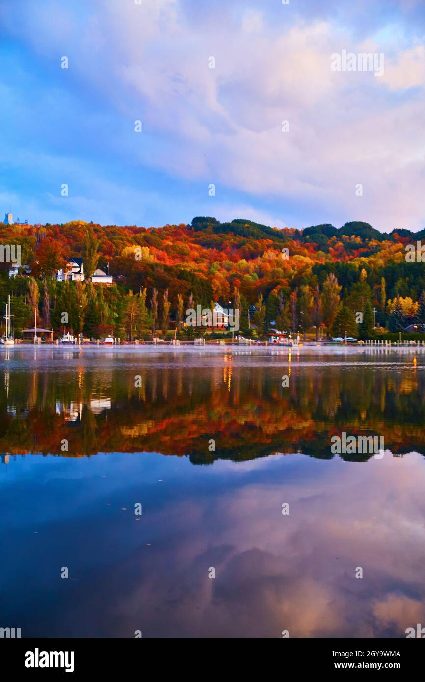 Caduta alberi di oro rosso arancio e verde sul lato opposto di un fiume riflesso nell'acqua con cielo blu e le nuvole viola all'alba Foto Stock