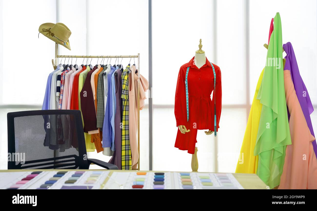 La stanza del designer di moda, la camicia rossa e il metro a nastro sono sul manichino. Un portabiti con tessuti colorati davanti alla grande finestra. Mattina Foto Stock