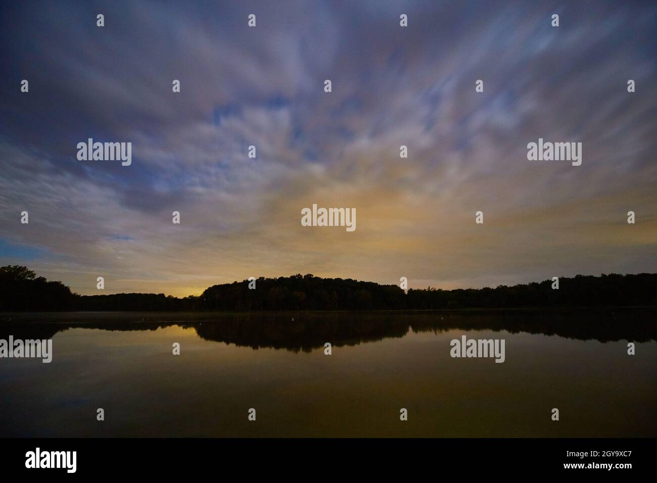 Cielo blu e giallo all'alba con un lago e una foresta al di là del lago Foto Stock