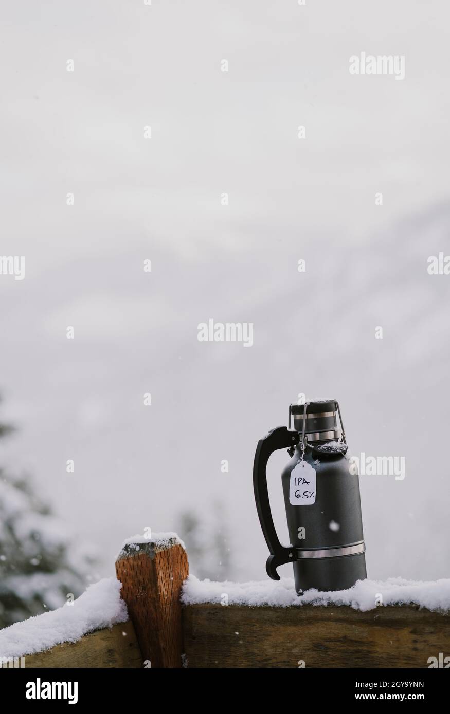 Un coltivatore pieno di birra fredda si siede su ringhiera di legno innevato all'esterno Foto Stock