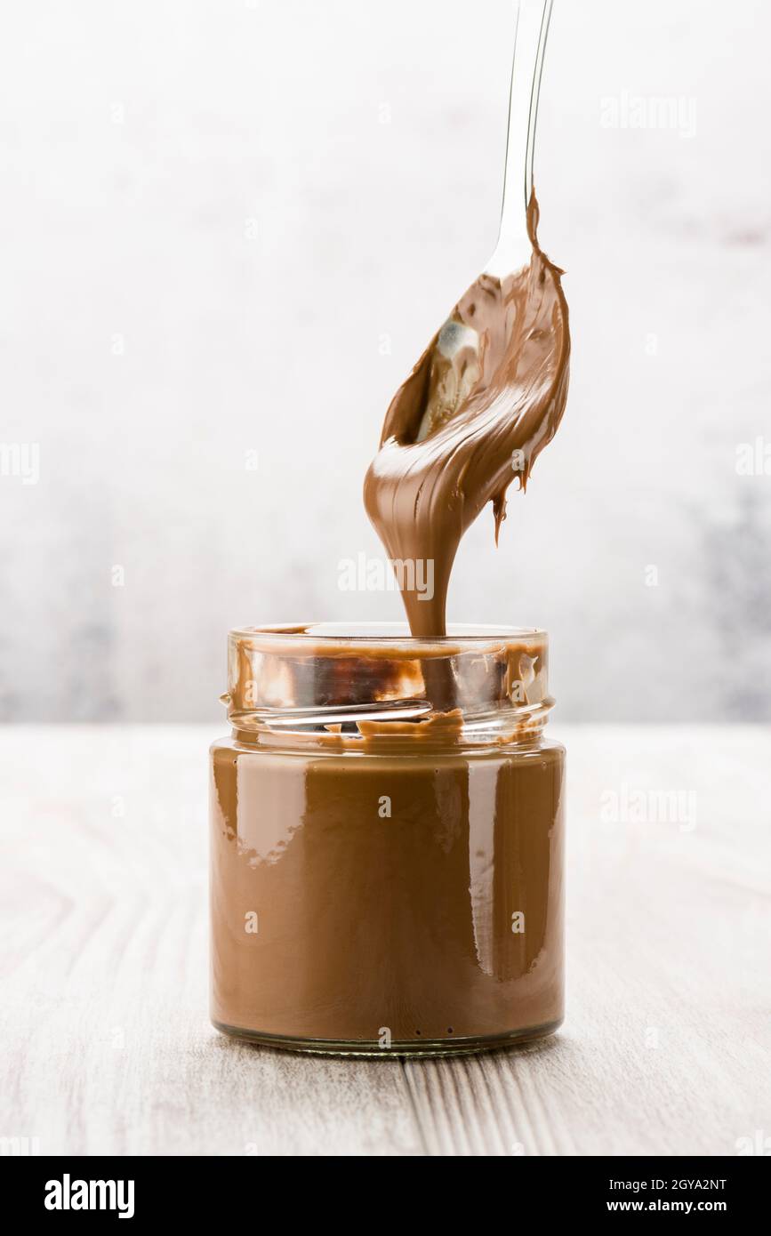 Crema di cioccolato in vaso di vetro con cucchiaio gocciolante, su tavolo di legno Foto Stock