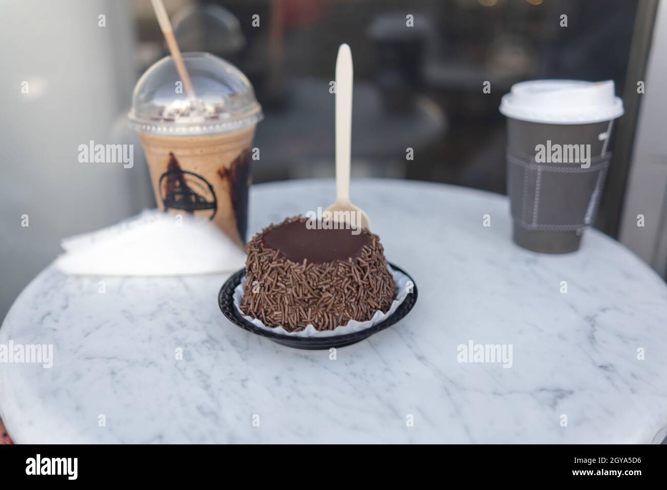 Frappuccino, piccola torta al cioccolato e tazza di caffè su tavola rotonda grigia Foto Stock