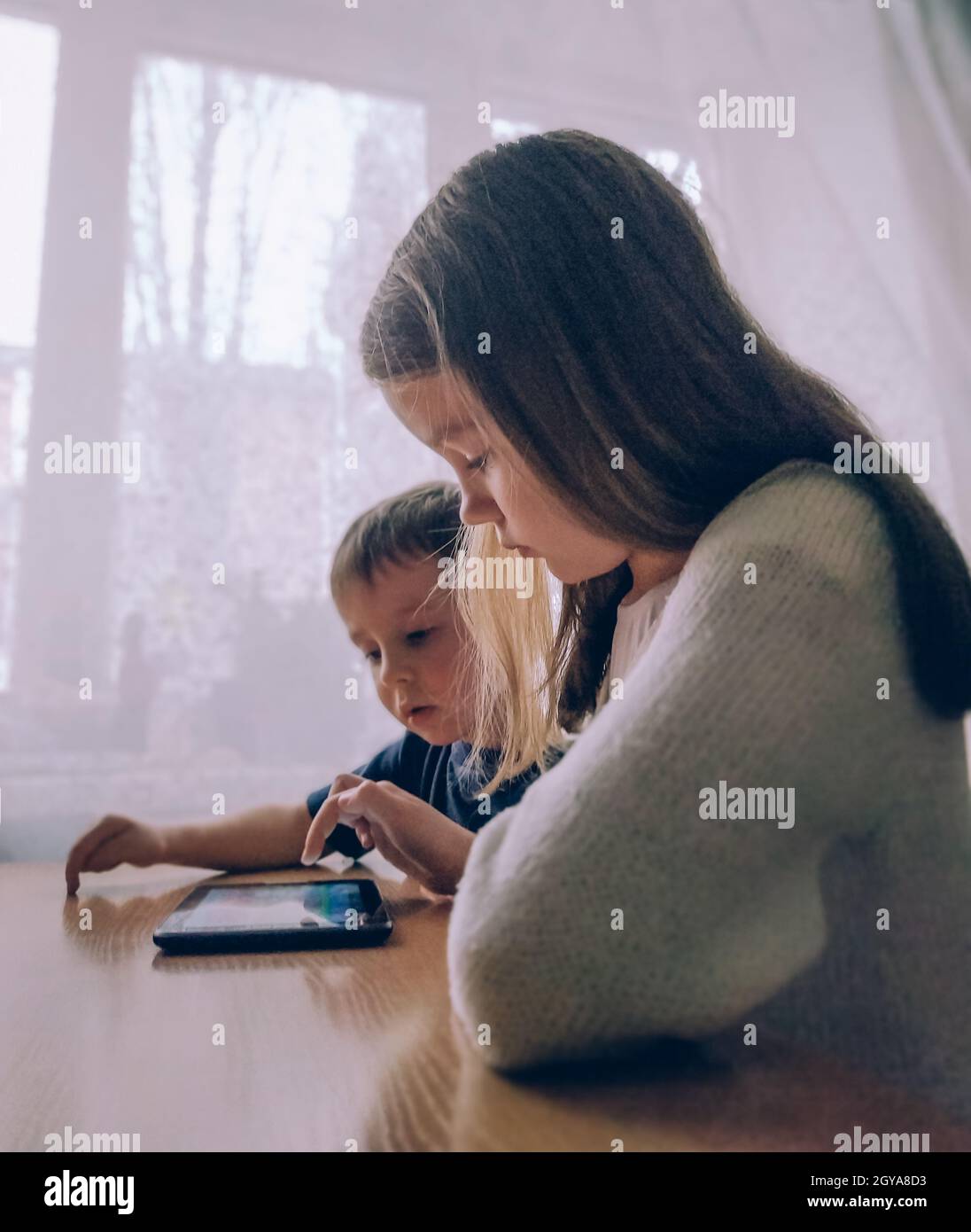 Bambina e ragazzo che giocano su un tablet PC gadget a casa al tavolo Foto Stock