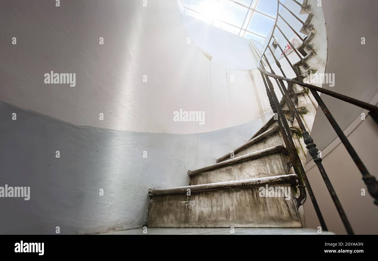 Antica scala a chiocciola con scalini in marmo e corrimano in ferro battuto. Luce naturale proveniente dal lucernario. Architettura e forma circolare Foto Stock