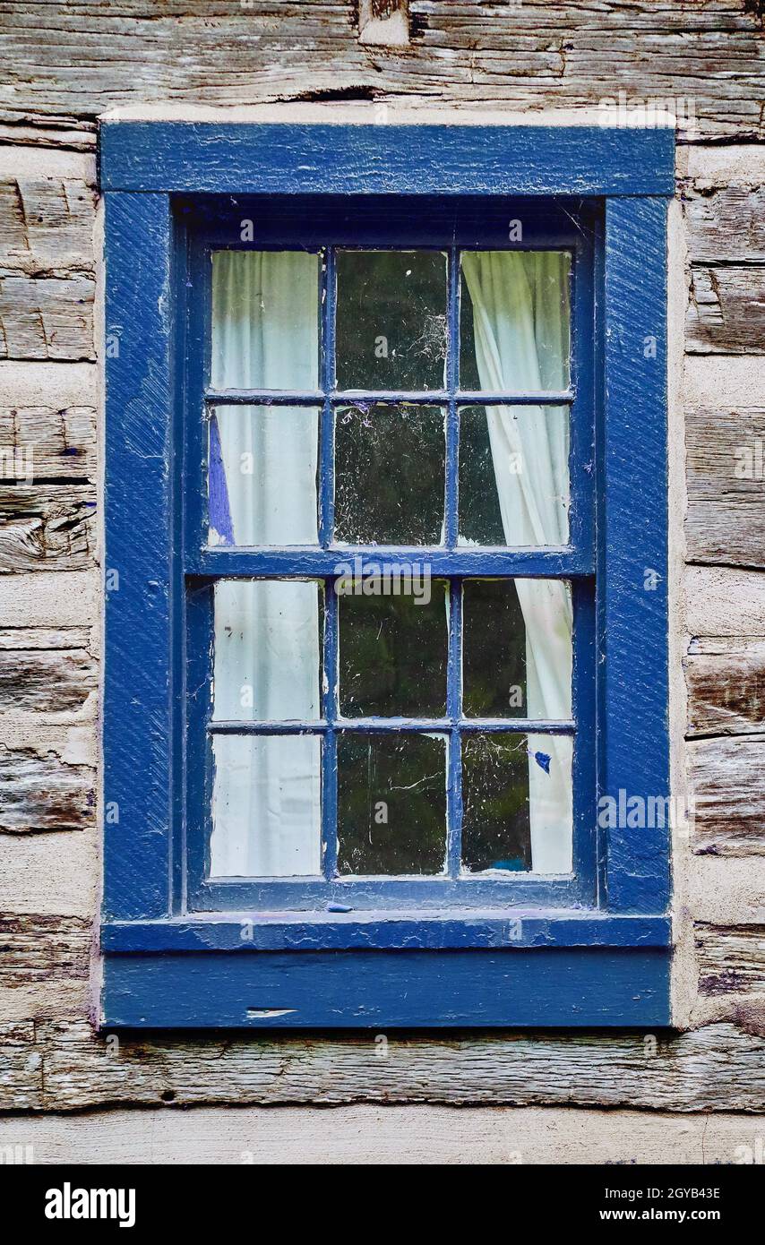 Vecchio edificio di legno chiaro sbiadito con una cornice di legno blu scuro e tende bianche tirate indietro Foto Stock