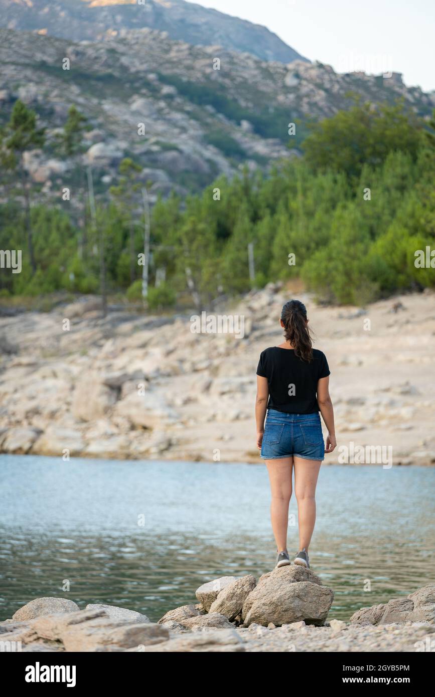Donna caucasica su un lago con montagne sullo sfondo a Vilarinho das Furnas Dam nel Parco Nazionale di Geres, in Portogallo Foto Stock