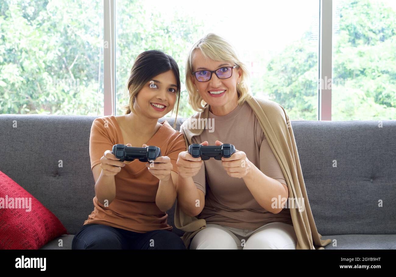 Happy mix pelle famiglia vivere insieme, figlia asiatica e la sua madre caucasica adottato giocare giochi console nel soggiorno. Foto Stock