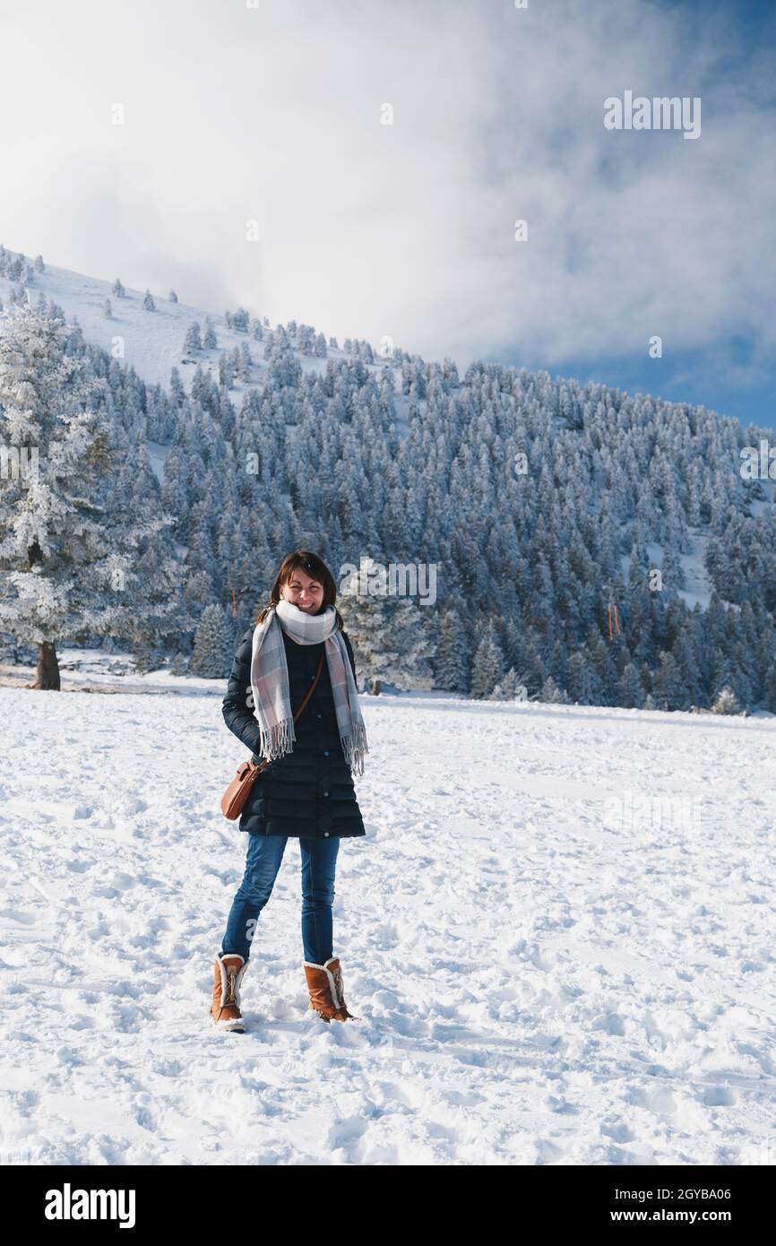Giovane donna caucasica sorridente in pista innevata che si gode di vacanze invernali presso la stazione sciistica con splendida vista sulle montagne innevate sullo sfondo. Vacanze invernali Foto Stock