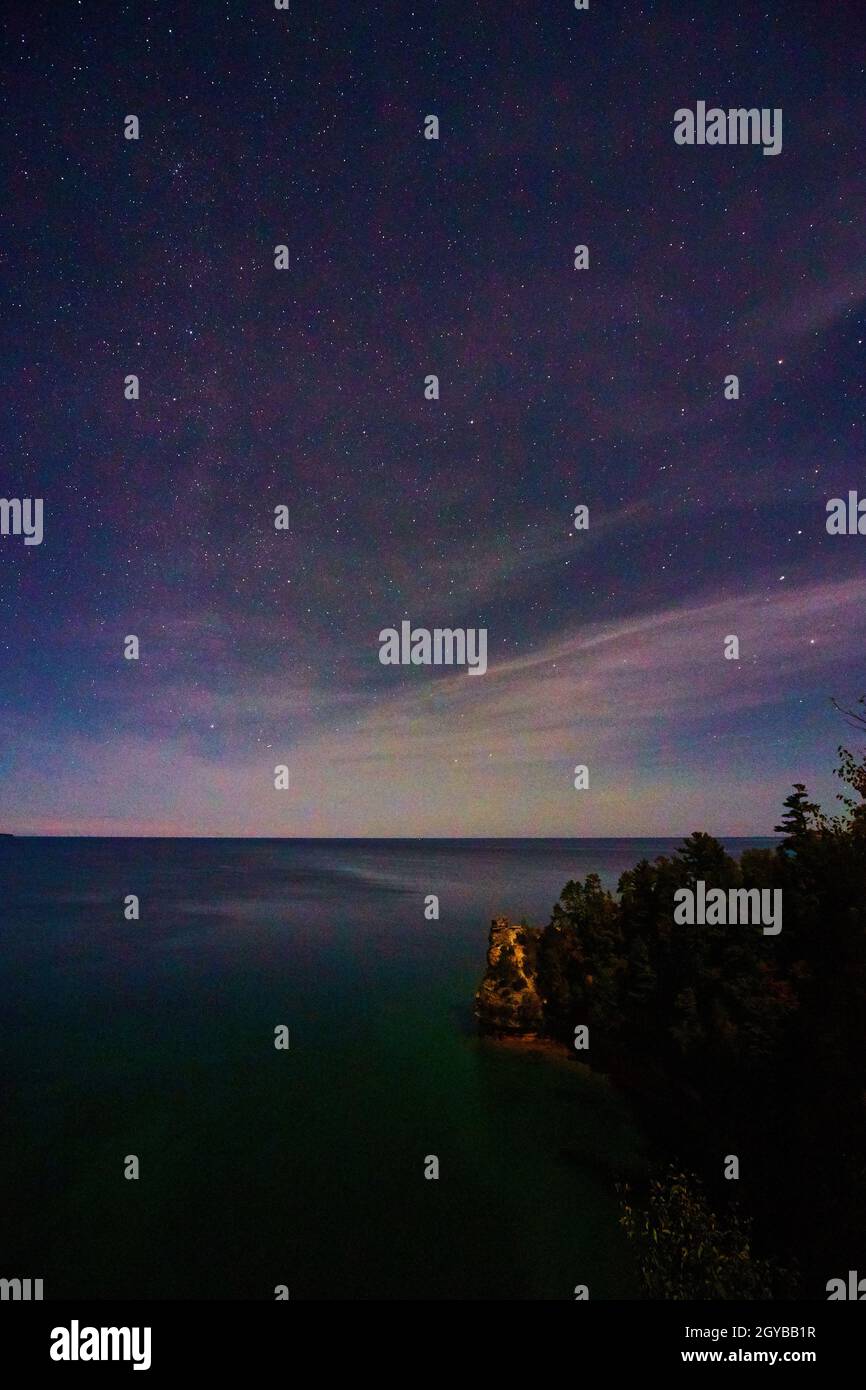 Cielo notturno con sussurri di morbide nuvole rosa sul lago Michigan e una scogliera con una foresta scura in basso a destra Foto Stock
