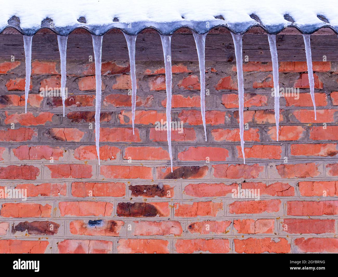 Ghiaccio di acqua ghiacciata sul tetto di una casa con un muro di mattoni. Scioglimento della neve. Inverno. Caduta della molla. Ghiaccio. Acqua congelata. Muro di mattoni. Frosty Fro Foto Stock