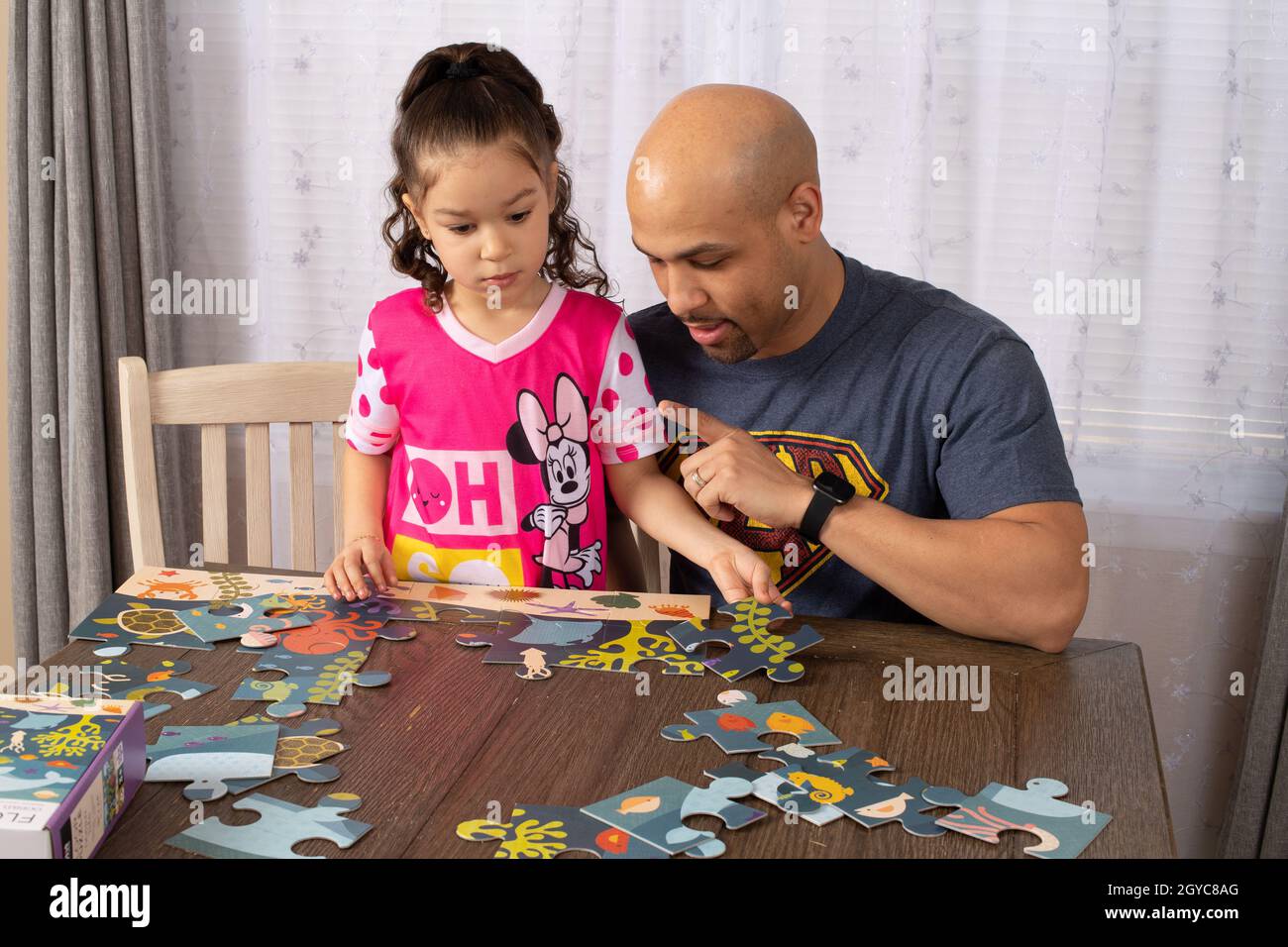 ragazza di 5 anni a casa con il padre, facendo puzzle insieme, il tema del puzzle è la vita dell'oceano Foto Stock