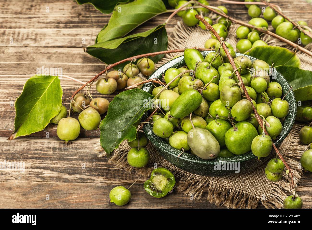 Raccolta di Actinidia arguta kiwi maturi in una ciotola di ceramica. Rami di frutta fresca kiwi con foglie verdi, vecchio sfondo in legno assi, spazio copia Foto Stock