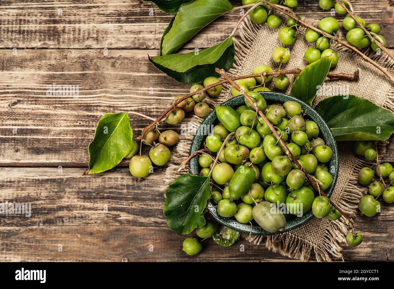 Raccolta di Actinidia arguta kiwi maturi in una ciotola di ceramica. Rami di frutta kiwi fresca con foglie verdi, vecchio sfondo in legno assi, vista dall'alto Foto Stock