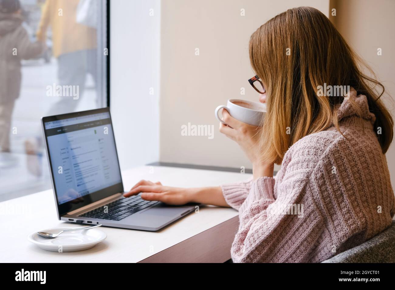 Giovane donna attraente che lavora su un portatile in uno spazio di lavoro moderno e bere cacao. Concetto di Elerning o freelance Foto Stock