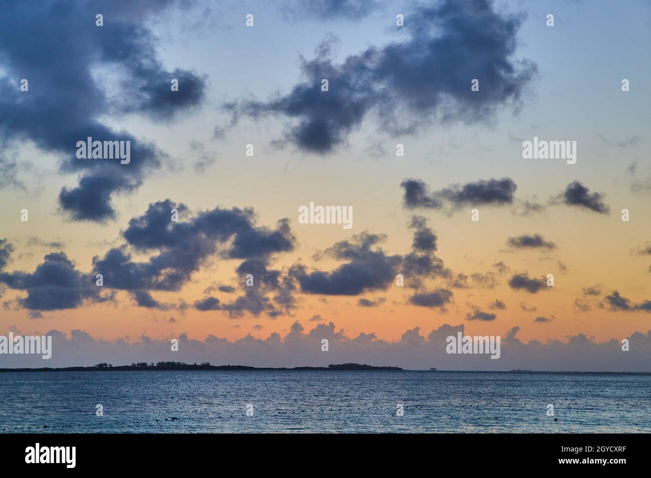 Tramonto sull'oceano con piccola isola e piccole nuvole scure Foto Stock