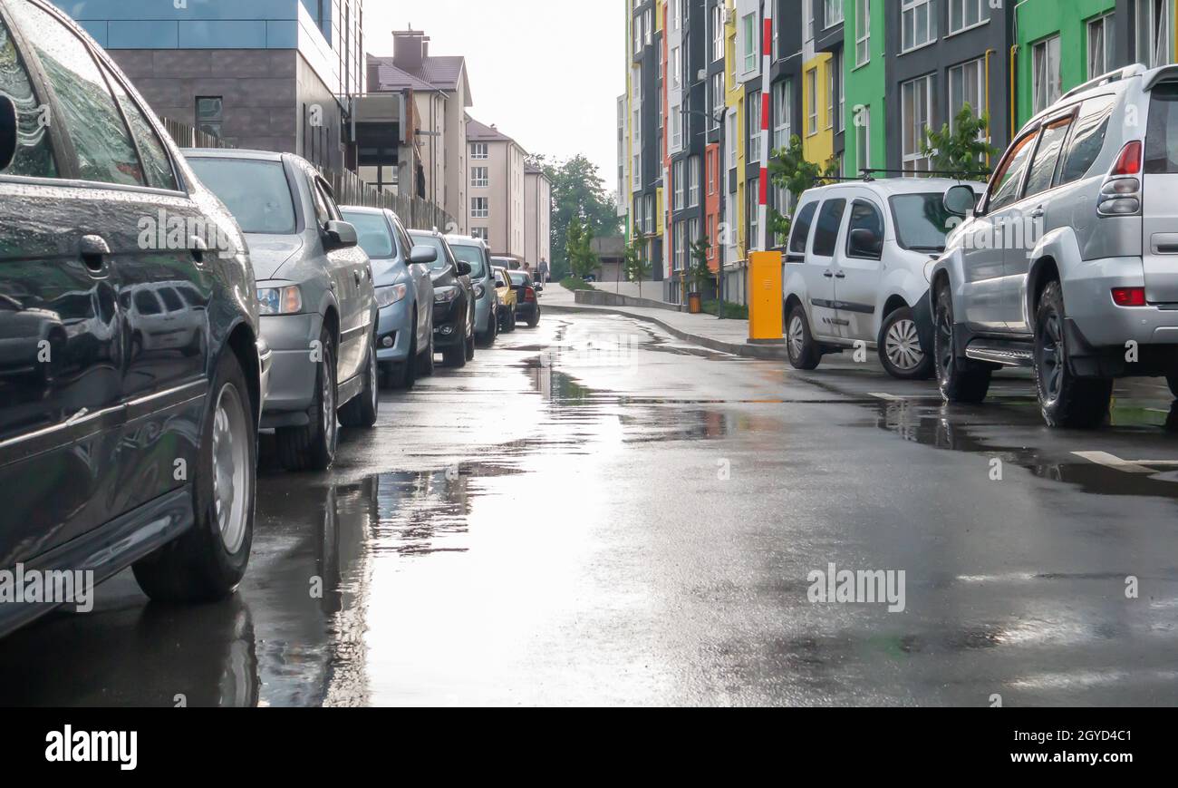 Strada in una città senza persone con auto parcheggiate in tempo piovoso. Pioggia sulla strada. Pioggia e auto. Sfondo di auto parcheggiate su una strada della città piovosa. Foto Stock