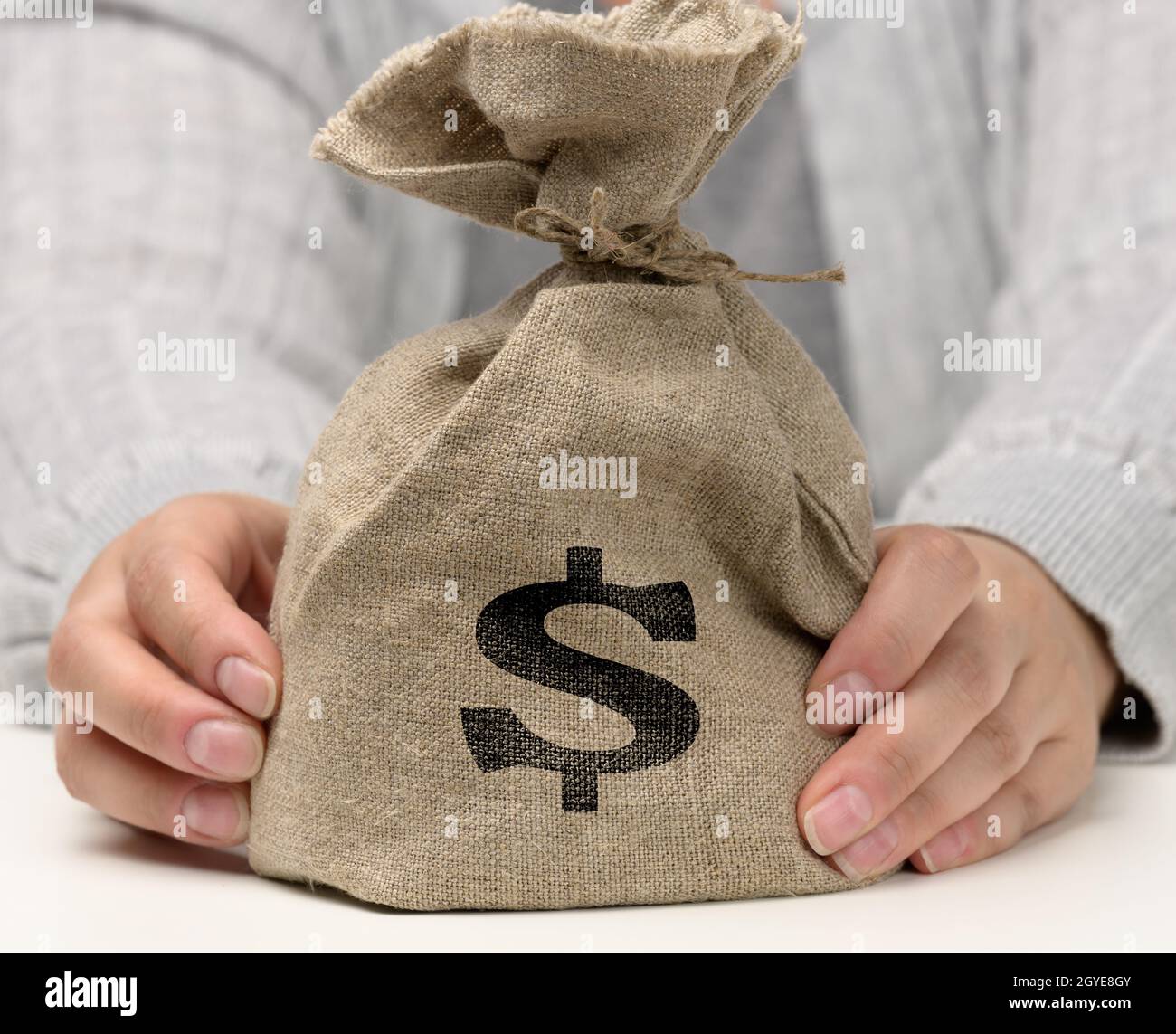 La mano tiene una borsa di tela piena di soldi con un'icona del dollaro degli Stati Uniti su uno sfondo bianco. Concetto di pianificazione del bilancio, profitto e risparmio, risultato finanziario finale Foto Stock