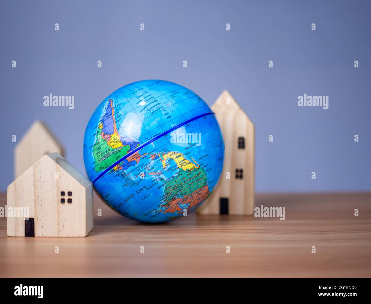 Una casa modello in legno è posta accanto ad un globo replica. Posto su un tavolo in legno con uno sfondo grigio chiaro. Salvare il concetto di mondo Foto Stock