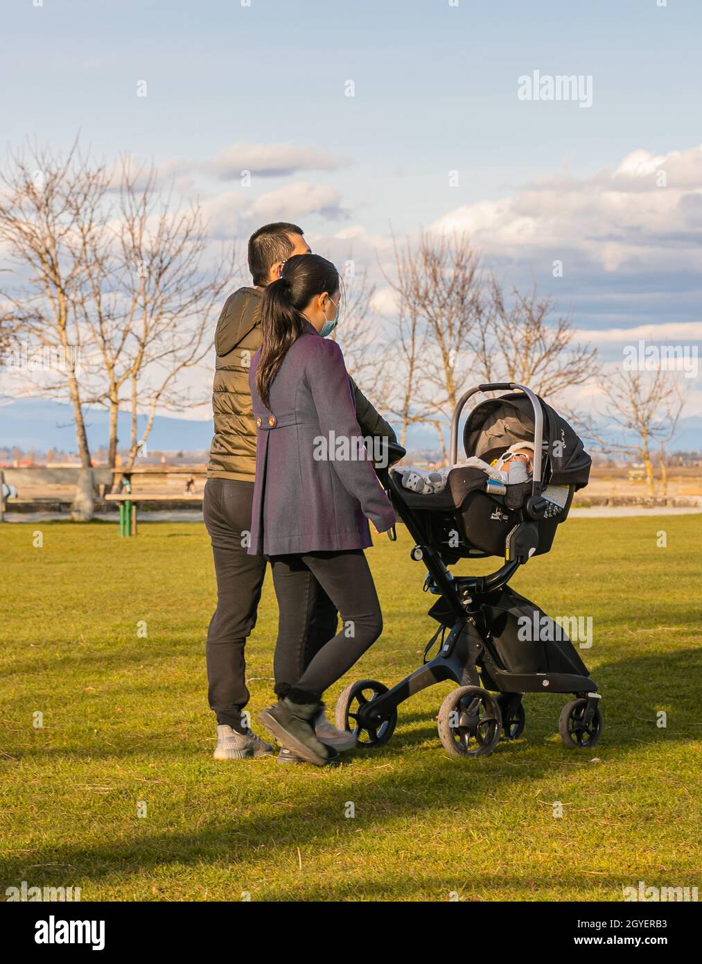 Coppia asiatica che cammina in un parco con il loro bambino in un passeggino cariage. Vista strada, foto di viaggio, messa a fuoco selettiva. White Rock, BC, Canada-8 aprile 2021 Foto Stock