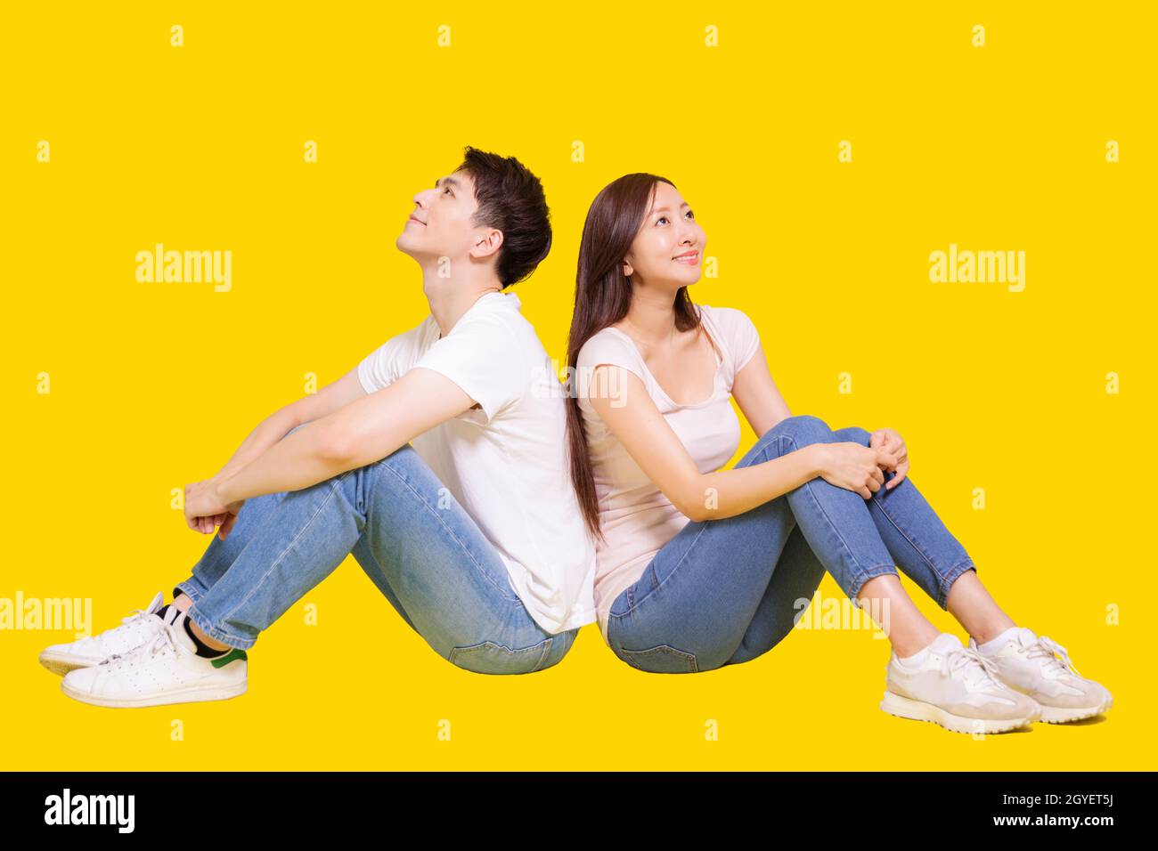 Giovane coppia seduta indietro a schiena e guardando sopra.isolato su sfondo giallo. Foto Stock