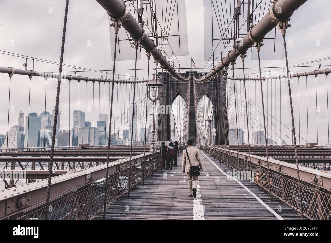 Uomo che cammina sul sentiero pedonale attraverso il ponte di Brooklyn. New York City Manhattan centro con grattacieli sul panorama dell'East River come visto da Brookly Foto Stock