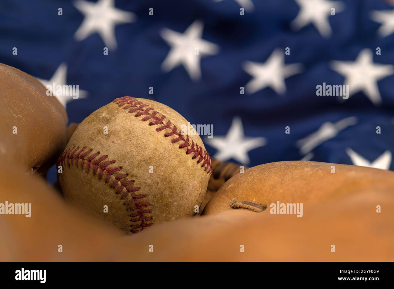 Il primo piano di un vecchio baseball e di un guanto contro la bandiera americana mette in evidenza uno degli sport più popolari del paese. Foto Stock