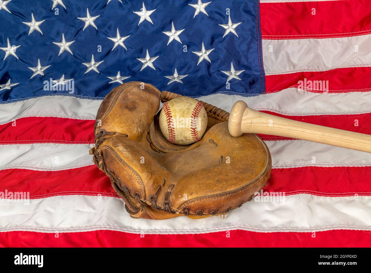 Il primo piano di un vecchio baseball e di un guanto contro la bandiera americana mette in evidenza uno degli sport più popolari del paese. Foto Stock