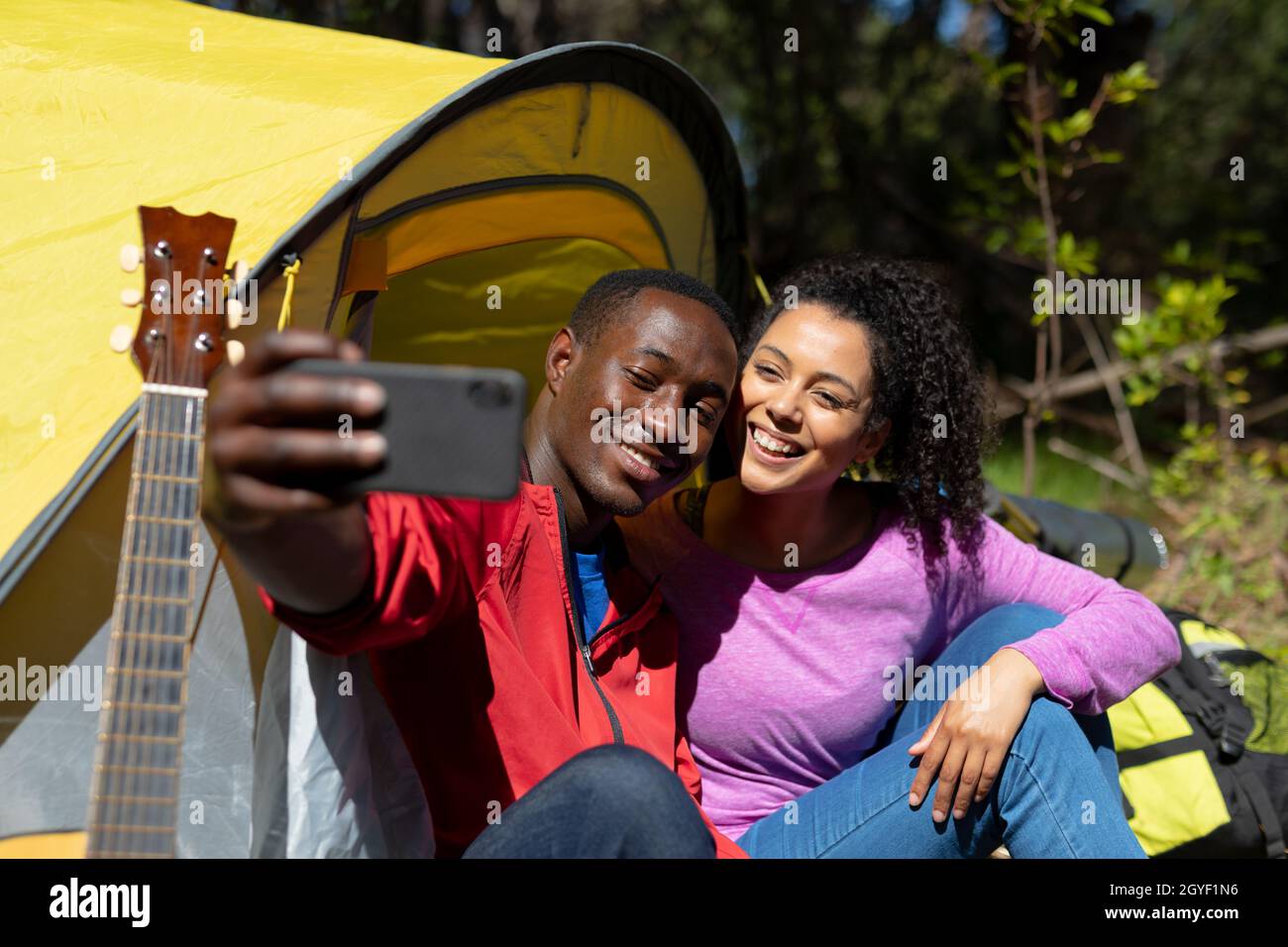Felice coppia variegata seduta nella tenda e prendere selfie in campagna Foto Stock